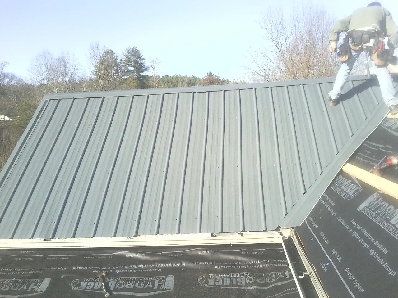 Crew installing dark green standing seam panels over synthetic underlayment in Dickson