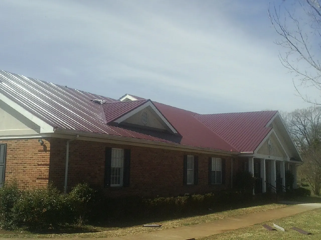 Red metal roof with gabled entries on a long brick building, from a Hail Damage Roof Repair job in Dickson