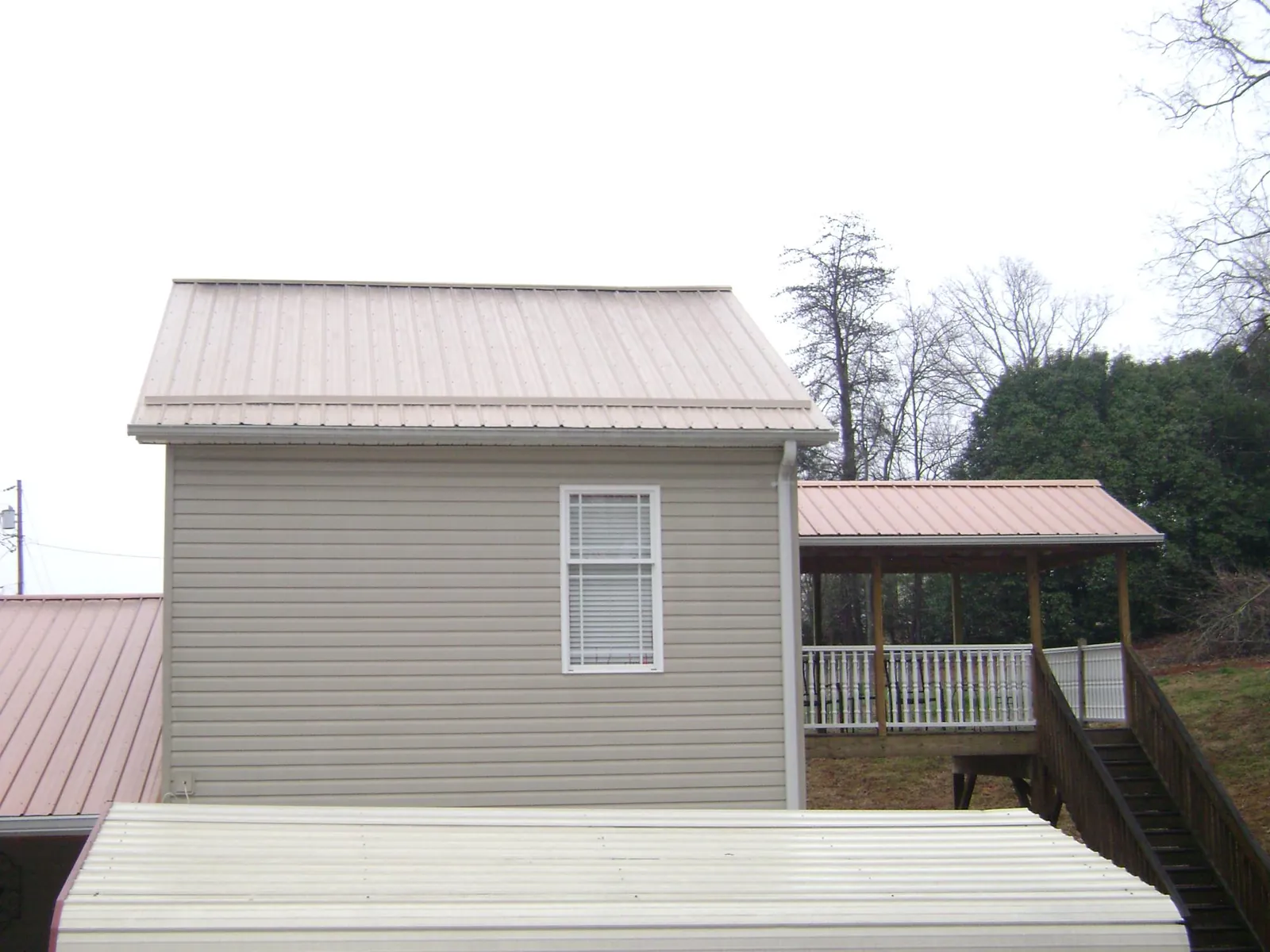 Tan metal roofs on a two story addition and attached porch, from a Roof Replacement job in Dickson